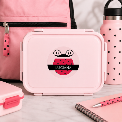 Pink lunch box with ladybug personalized label design  surrounded by pink backpack, water bottle, and notebook.