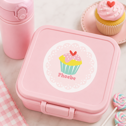 Personalized cupcake waterproof name label on a pastel pink lunch box with matching pink water bottle, cupcake-themed props, and coordinated school accessories.